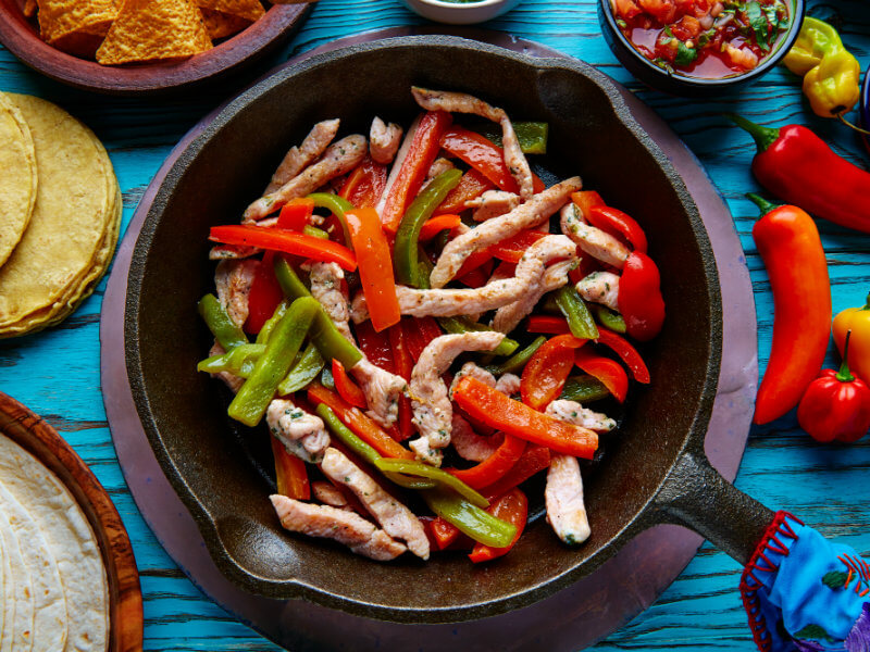 Fajitas de pollo con pimientos y champiñones cocinadas en un sartén