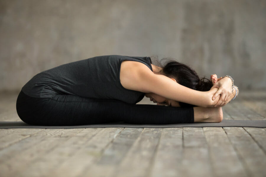 Mujer haciendo postura de la pinza sentada paschimottanasana